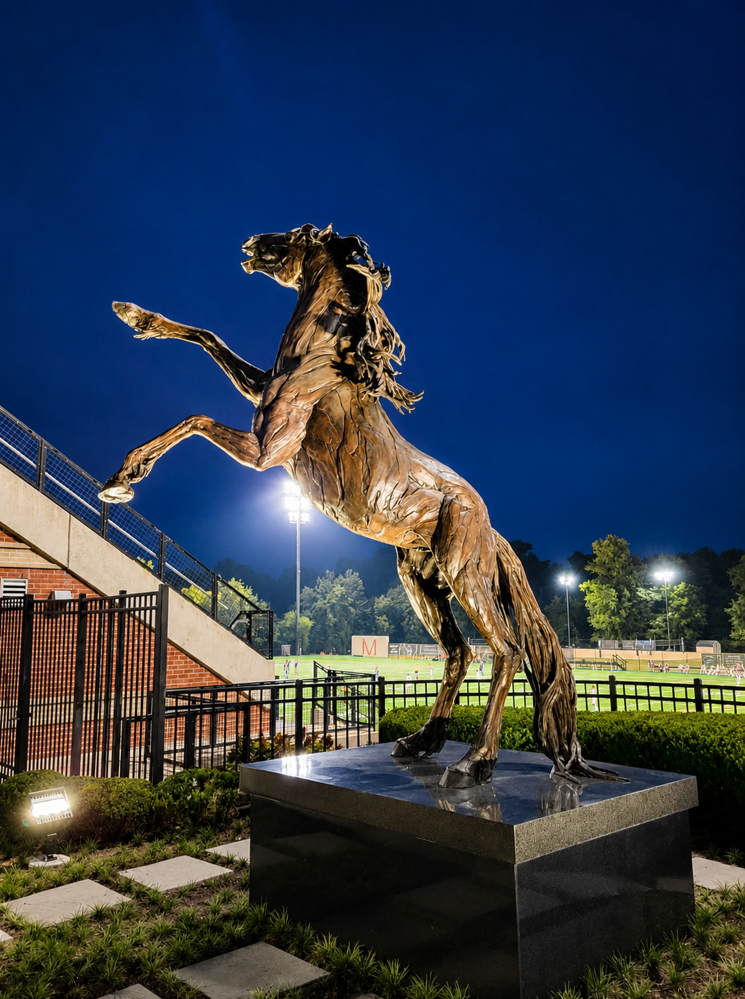 Bronze horse sculpture lit at night with stadium and field lighting at Stevenson University