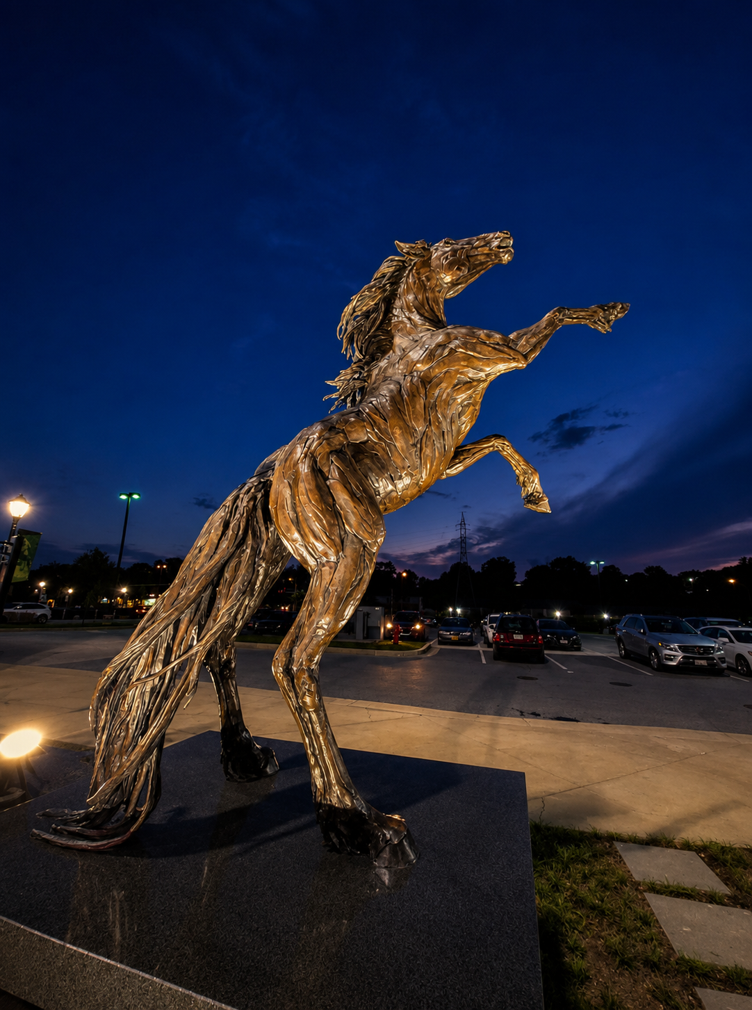 Golden bronze horse sculpture illuminated at dusk with parking lot lighting at Stevenson University