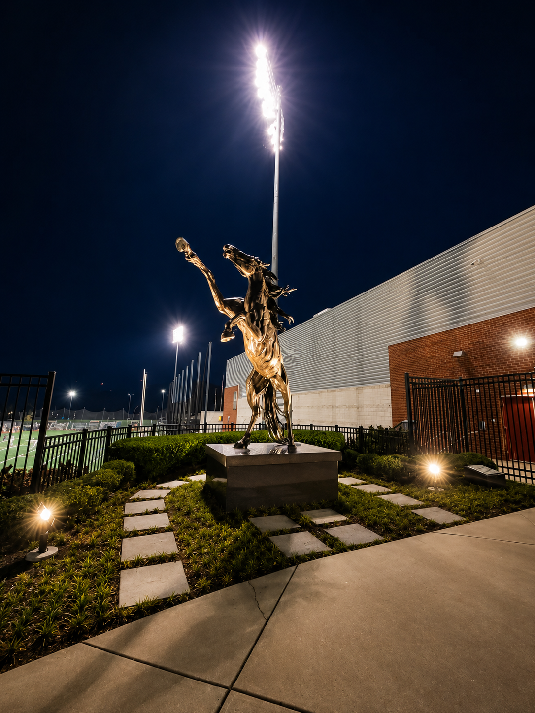 Wide shot of illuminated horse sculpture with field lighting poles and stadium building at Stevenson University